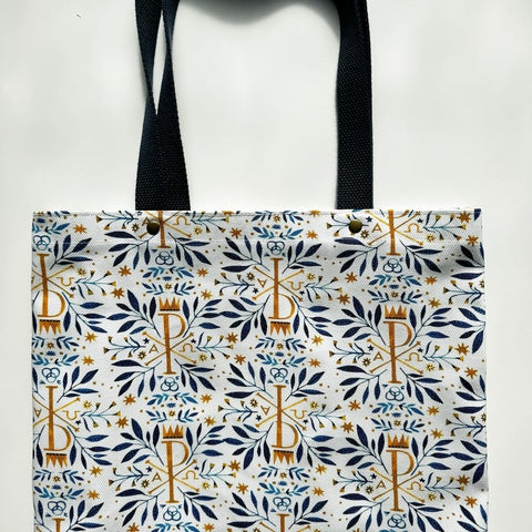 Unlined tote bag measuring approximately 13” wide x 15” tall. Exterior fabric features white background with beautiful navy watercolor floral print along with gold Chi Rho Christogram. Navy cotton webbing straps.