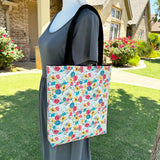 Lined tote bag measuring approximately 12" wide x 14" tall x 2.5" deep. Exterior fabric features white background with bright watercolor flowers and a hidden rosary design. Black lining. Black cotton webbing straps.