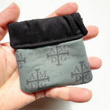 Clasp pouch measuring approximately 3.75” wide x 3.5” wall x 1” deep. Outer fabric is a Dark green background with black AMDG images. Inside lining is a black fabric. Clasp frame for easy opening and closing.