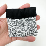 Squeeze pouch measuring approximately 3.25" tall x 3.25" wide. Outer fabric is a black and white floral print with Latin text of the Hail Mary dispersed throughout. Inside accent is a black fabric. Snap frame for easy opening and closing.