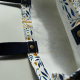 Unlined tote bag measuring approximately 13” wide x 15” tall. Exterior fabric features white background with beautiful navy watercolor floral print along with gold Chi Rho Christogram. Navy cotton webbing straps.