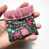 Clasp pouch measuring approximately 3.75” wide x 3.5” wall x 1” deep. Outer fabric is a bright and cheery black floral background with the words of the Hail Mary interspersed throughout. Inside lining is a pink fabric with cross stitch embroidery design. Clasp frame for easy opening and closing.