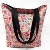 Lined tote bag measuring approximately 12" wide x 14" tall x 2.5" deep. Exterior fabric features bright and cheery pink floral background with the words of the Hail Mary interspersed throughout. Black lining. Black cotton webbing straps.