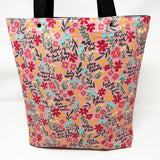 Lined tote bag measuring approximately 12" wide x 14" tall x 2.5" deep. Exterior fabric features bright and cheery pink floral background with the words of the Hail Mary interspersed throughout. Black lining. Black cotton webbing straps.