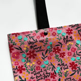 Unlined tote bag measuring approximately 13” wide x 15” tall. Exterior fabric features bright and cheery pink floral background with the words of the Hail Mary interspersed throughout. Black cotton webbing straps.