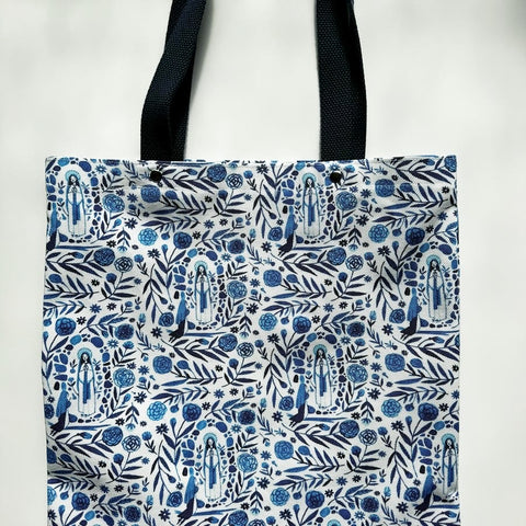 Unlined tote bag measuring approximately 13” wide x 15” tall. Exterior fabric features gorgeous blue floral print with images of Our Lady of Lourdes. Navy cotton webbing straps.