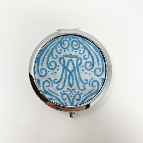 Light blue background with turquoise print along with Auspice Maria monogram; 3 compartment silver pill box
